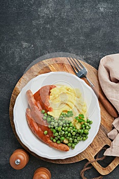 Bangers and mash. Grilled sausages with mash potato and green pea on white plate on black dark background. Traditional dish of