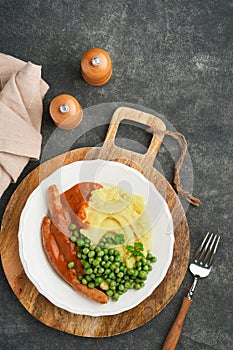 Bangers and mash. Grilled sausages with mash potato and green pea on white plate on black dark  background. Traditional dish of Gr