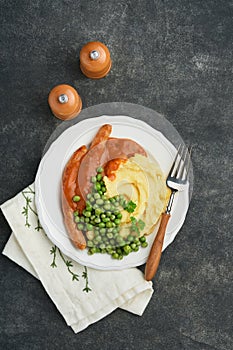 Bangers and mash. Grilled sausages with mash potato and green pea on white plate on black dark  background. Traditional dish of Gr