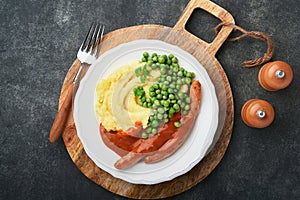 Bangers and mash. Grilled sausages with mash potato and green pea on white plate on black dark  background. Traditional dish of Gr