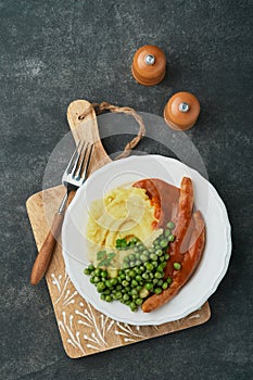 Bangers and mash. Grilled sausages with mash potato and green pea on white plate on black dark  background. Traditional dish of Gr