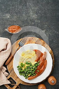 Bangers and mash. Grilled sausages with mash potato and green pea on white plate on black dark  background. Traditional dish of Gr