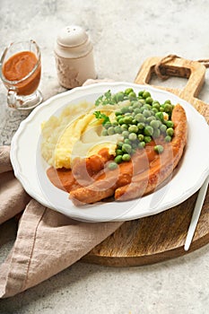 Bangers and mash. Grilled sausages with mash potato and green pea on white plate on grey background. Traditional dish of Great