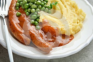 Bangers and mash. Grilled sausages with mash potato and green pea on white plate on grey background. Traditional dish of Great