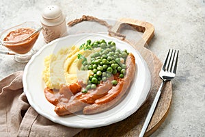 Bangers and mash. Grilled sausages with mash potato and green pea on white plate on grey background. Traditional dish of Great