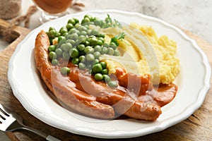Bangers and mash. Grilled sausages with mash potato and green pea on white plate on grey background. Traditional dish of Great