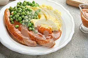 Bangers and mash. Grilled sausages with mash potato and green pea on white plate on grey background. Traditional dish of Great Bri