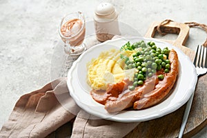 Bangers and mash. Grilled sausages with mash potato and green pea on white plate on grey background. Traditional dish of Great Bri