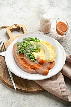 Bangers and mash. Grilled sausages with mash potato and green pea on white plate on grey background. Traditional dish of Great Bri