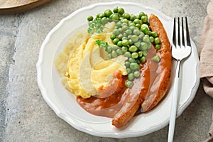 Bangers and mash. Grilled sausages with mash potato and green pea on white plate on grey background. Traditional dish of Great Bri