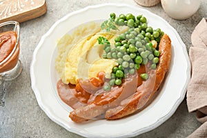 Bangers and mash. Grilled sausages with mash potato and green pea on white plate on grey background. Traditional dish of Great Bri