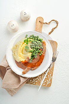 Bangers and mash. Grilled sausages with mash potato and green pea on white plate on light background. Traditional dish of Great