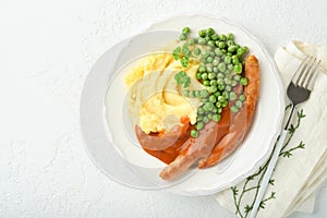 Bangers and mash. Grilled sausages with mash potato and green pea on white plate on light background. Traditional dish of Great Br