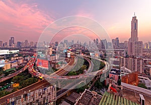 Bangkok at rosy dusk with skyscrapers in background and busy traffic on elevated expressways & circular interchanges