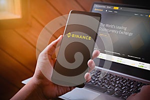 Bangkok, Thailand - August 5, 2019: Hands holding Smartphone with binance logo on screen and binance website on laptop background