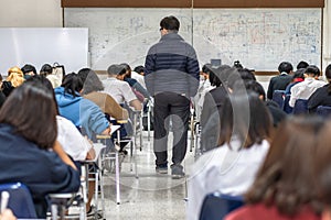 School exam room with teacher invigilator monitoring students taking educational examination in classroom for admission test