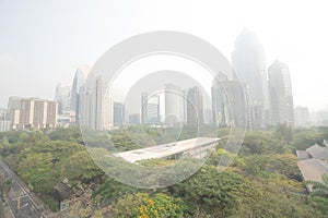 BANGKOK, THAILAND JAN 21, 2019 ; Bangkok skycrapper office building gray out covered by PM 2.5 dust with green tree in public park