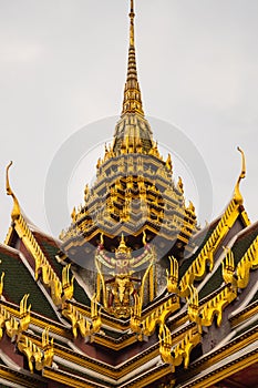 Bangkok, Thailand - January 25, 2016: Detail of one of the roofs decorated in gold in the grand palace of Bangkok with a statue of