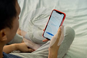 BANGKOK,THAILAND - MARCH 27, 2020: A man holding a phone with screen shot of ZOOM Cloud Meetings app on iPhone. Zoom