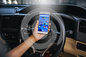 BANGKOK, THAILAND - NOVEMBER 12th, 2017 : Hand of woman using mobile phone with icons of social media on screen in the car