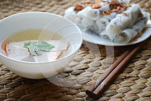 Banh cuon-vietnamese steamed rice rolls with minced meat inside and pieces of vietnamese ham accompanied by bowl of fish sauce.