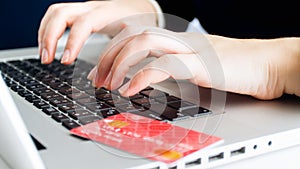 Bank credit card lying on laptop next to female hands typing on keyboard. Concept of online shopping and e-commerce