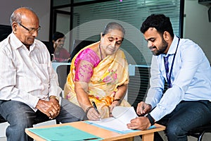 bank employee taking sign from retired senior couple at office for insurence or loan documents - concept of banking