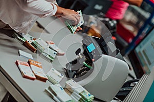 Bank employees using money counting machine while sorting and counting paper banknotes inside bank vault. Large amounts