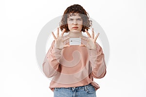 Bank and finance concept. Angry and confused girl frowns, shows credit card in hands, looks disappointed at camera