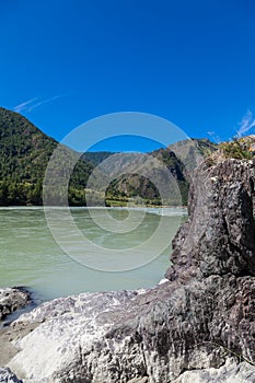 The bank of the Katun river with water containing turquoise clay and a sandy beach, rocky coast against the backdrop of mountains