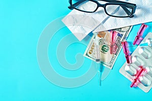 Banknote of 100 usd, glasses, pills, vaccine and syringe on green background