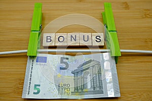 A banknote hanging by a thread with two green clothespins,on a wooden plank with bonus written. Concept of  bonus for housewives
