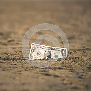 Banknote of value of one dollar in the the sand on the beach. Concept of cheap travel and vacation.