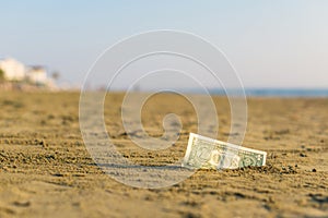 Banknote of value of one dollar in the the sand on the beach. Concept of cheap travel and vacation.