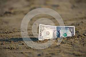 Banknote of value of one dollar in the the sand on the beach. Concept of cheap travel and vacation.
