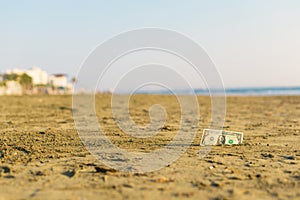 Banknote of value of one dollar in the the sand on the beach. Concept of cheap travel and vacation.