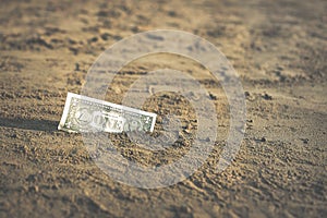 Banknote of value of one dollar in the the sand on the beach. Concept of cheap travel and vacation.