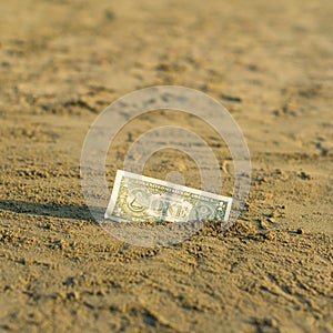 Banknote of value of one dollar in the the sand on the beach. Concept of cheap travel and vacation.