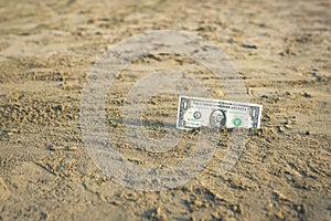 Banknote of value of one dollar in the the sand on the beach. Concept of cheap travel and vacation.