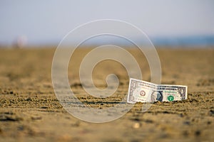 Banknote of value of one dollar in the the sand on the beach. Concept of cheap travel and vacation.