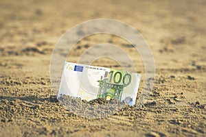 Banknote of value of one hundred euro in the the sand on the beach. Concept of cheap travel and vacation.