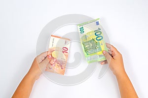 Banknotes of 10 and 100 euros in children`s hands on a white table