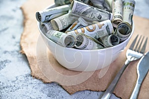 Banknotes of American cash dollar bills of various denominations are poured into a plate as a symbol of the high cost of organic