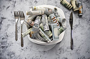 Banknotes of American dollar bills of various denominations are poured into a plate as a symbol of consumption of cash resources