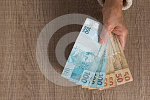 Banknotes of brazilian currency: Reais. Top view of old woman`s hand handling bills
