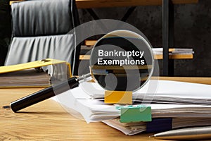 Bankruptcy exemptions concept. A magnifying glass lies on a stack of papers.