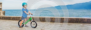 BANNER Active blond kid boy driving bicycle in the park near the sea. Toddler child dreaming and having fun on warm summer day. ou