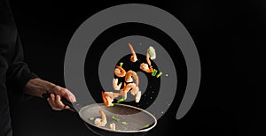 Banner, advertising. Cooking shrimp with vegetables, seafood in a pan. Professional cooking by the chef on a black background. photo