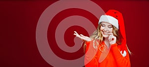 banner. a beautiful woman in a Santa Claus hat points hand to a red background.