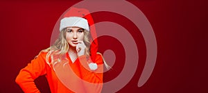 banner. a beautiful woman in a Santa Claus hat thinks on a red background.